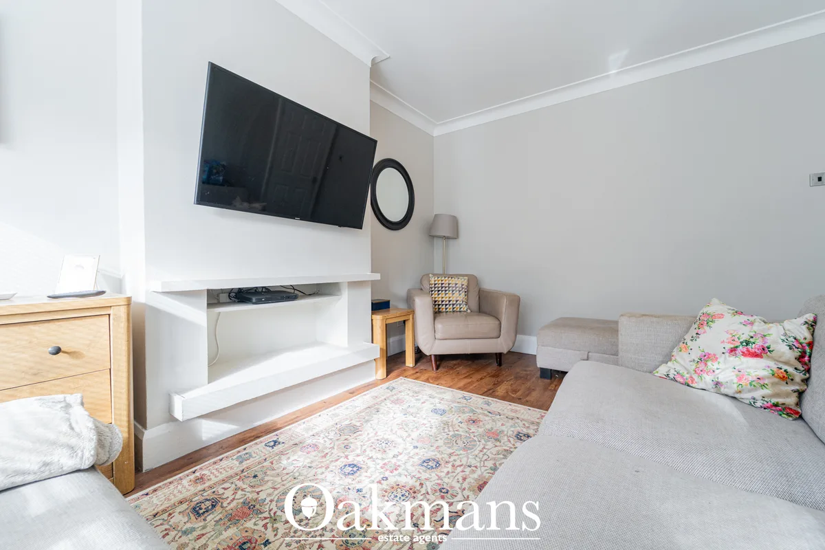 Bright living room with wall-mounted TV, cream armchair, grey sofa, patterned rug, wooden furniture and neutral décor