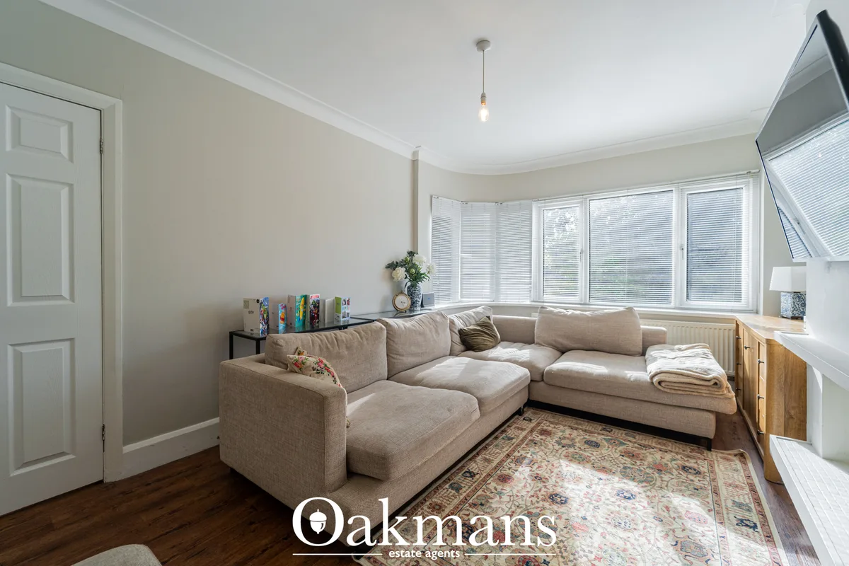 Bright living room with cream L-shaped sofa, bay windows with blinds, wooden flooring, patterned rug, pendant lighting a