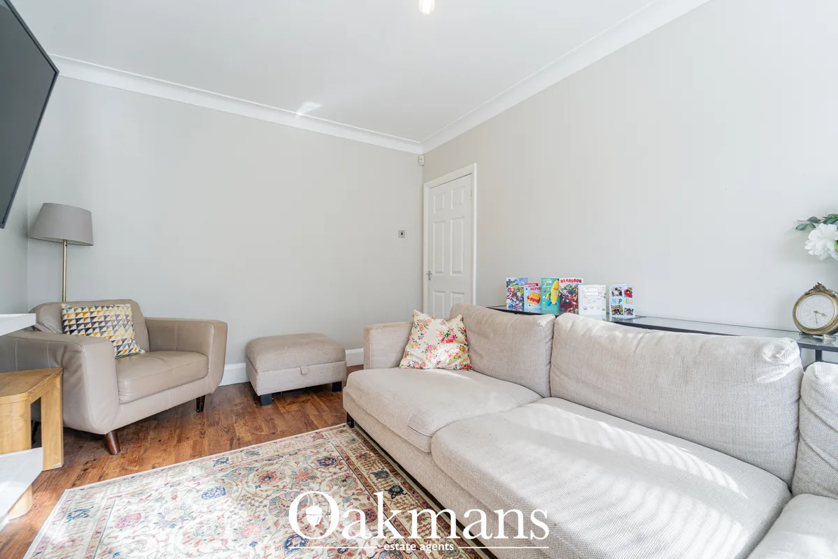 Spacious living room with beige L-shaped sofa, matching armchair, cream walls, wooden flooring, patterned rug and recess