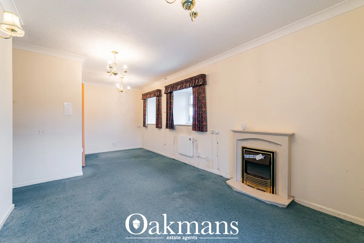Spacious living room with cream walls, fireplace with stone surround, two windows with patterned curtains, ceiling light