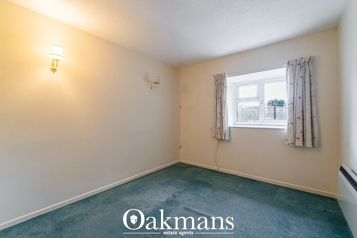 Empty bedroom with cream walls, green carpet, double window with floral curtains, wall-mounted lighting and radiator