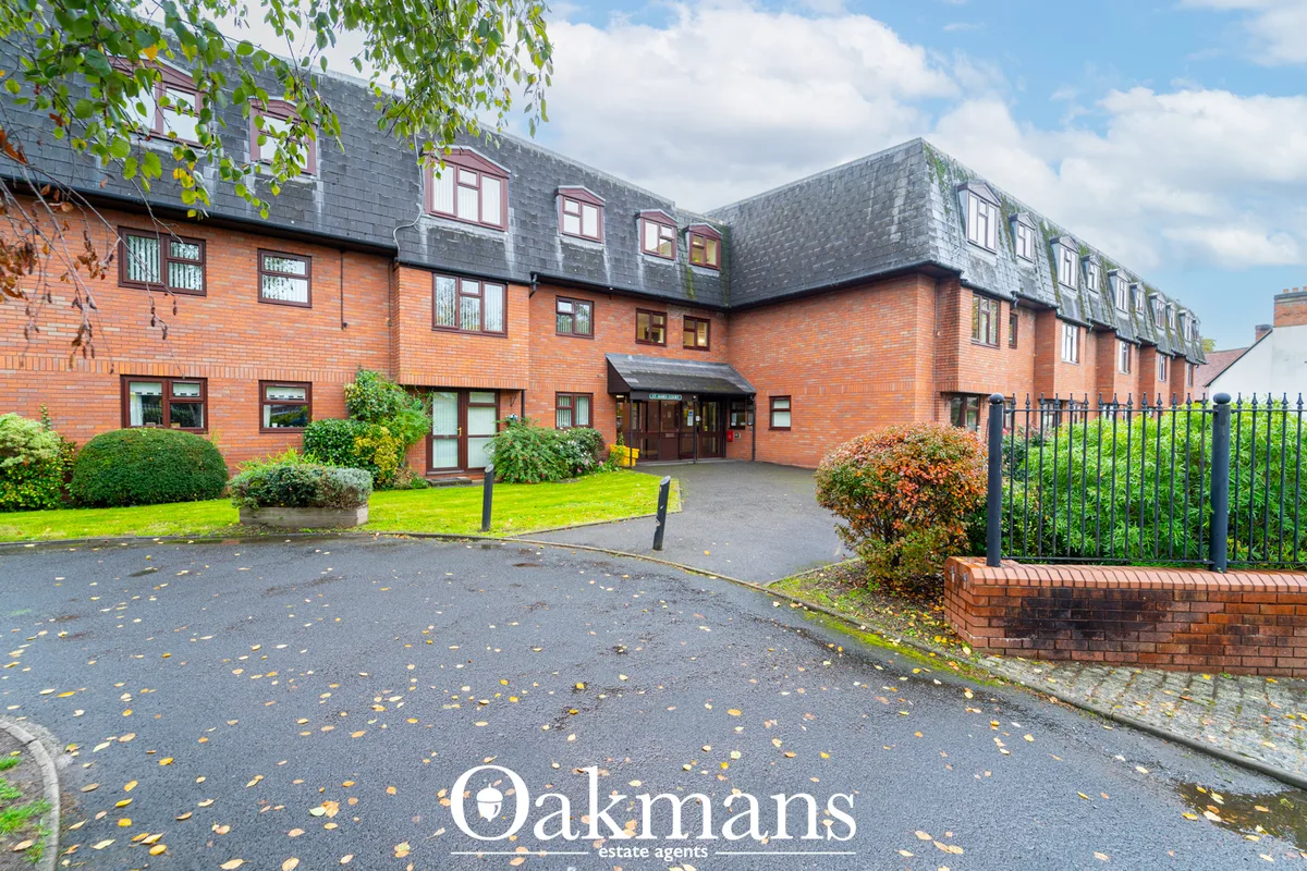 Red brick residential building with slate roof, manicured lawns, topiary hedges, and formal driveway entrance