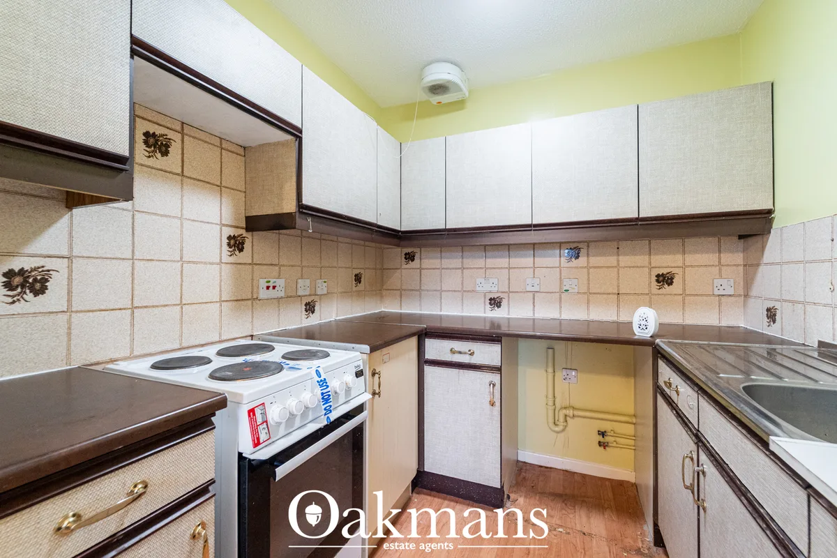 Kitchen with cream and brown units, beige tiled walls, electric cooker, sink, yellow ceiling and wood flooring