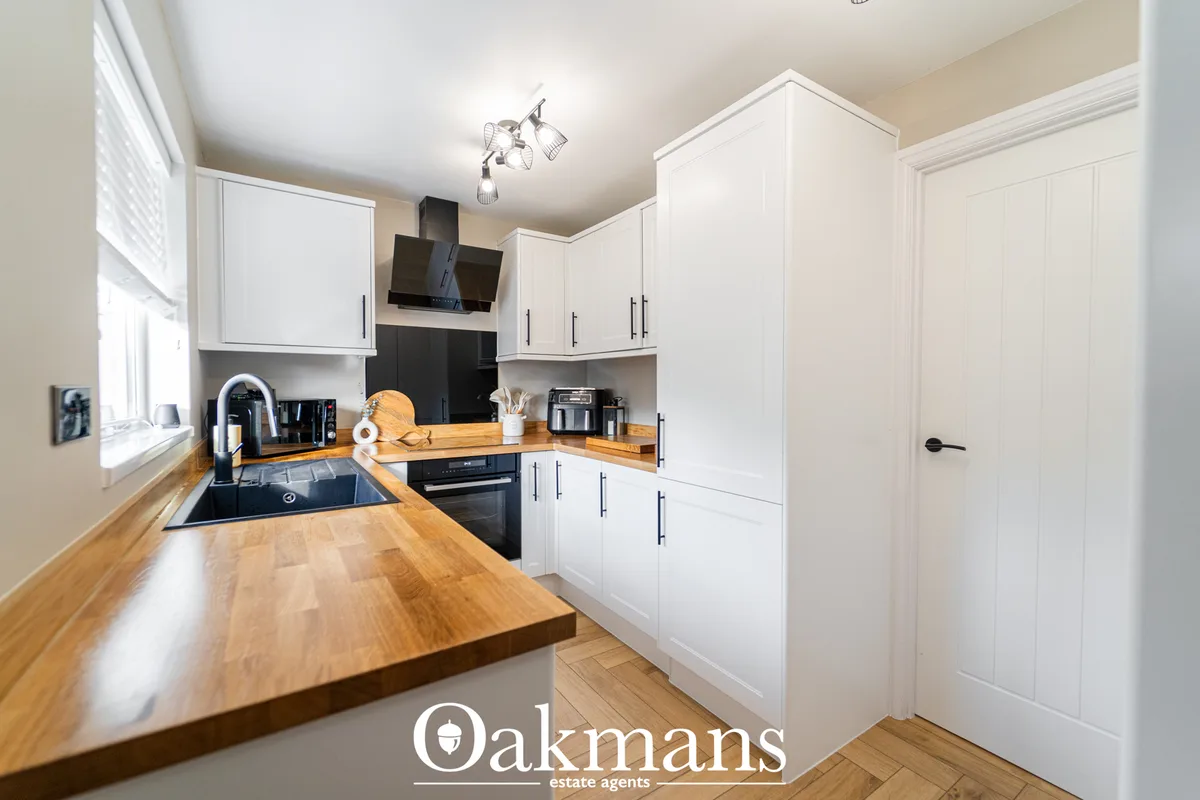Modern fitted kitchen with white cabinetry, wooden worktops, black appliances, induction hob and range hood