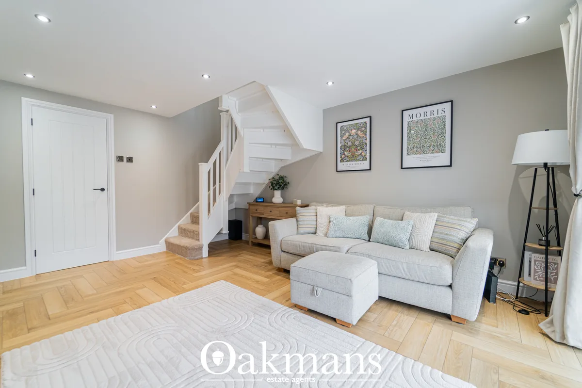 Bright living room with cream upholstered sofa, wooden side table, framed art prints, white staircase with wooden steps,