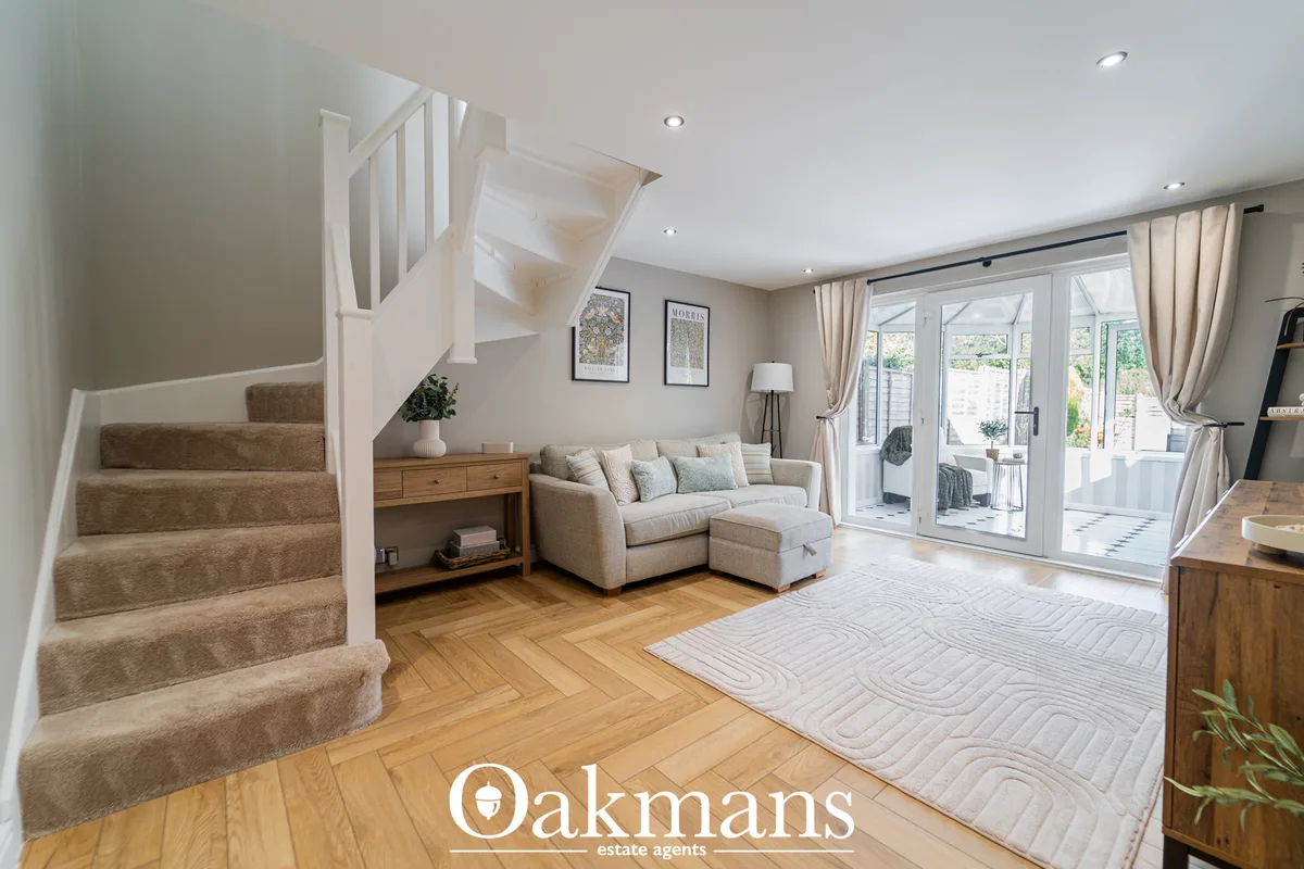 Bright open-plan living room with beige corner sofa, wooden console table, herringbone flooring, glass patio doors and s