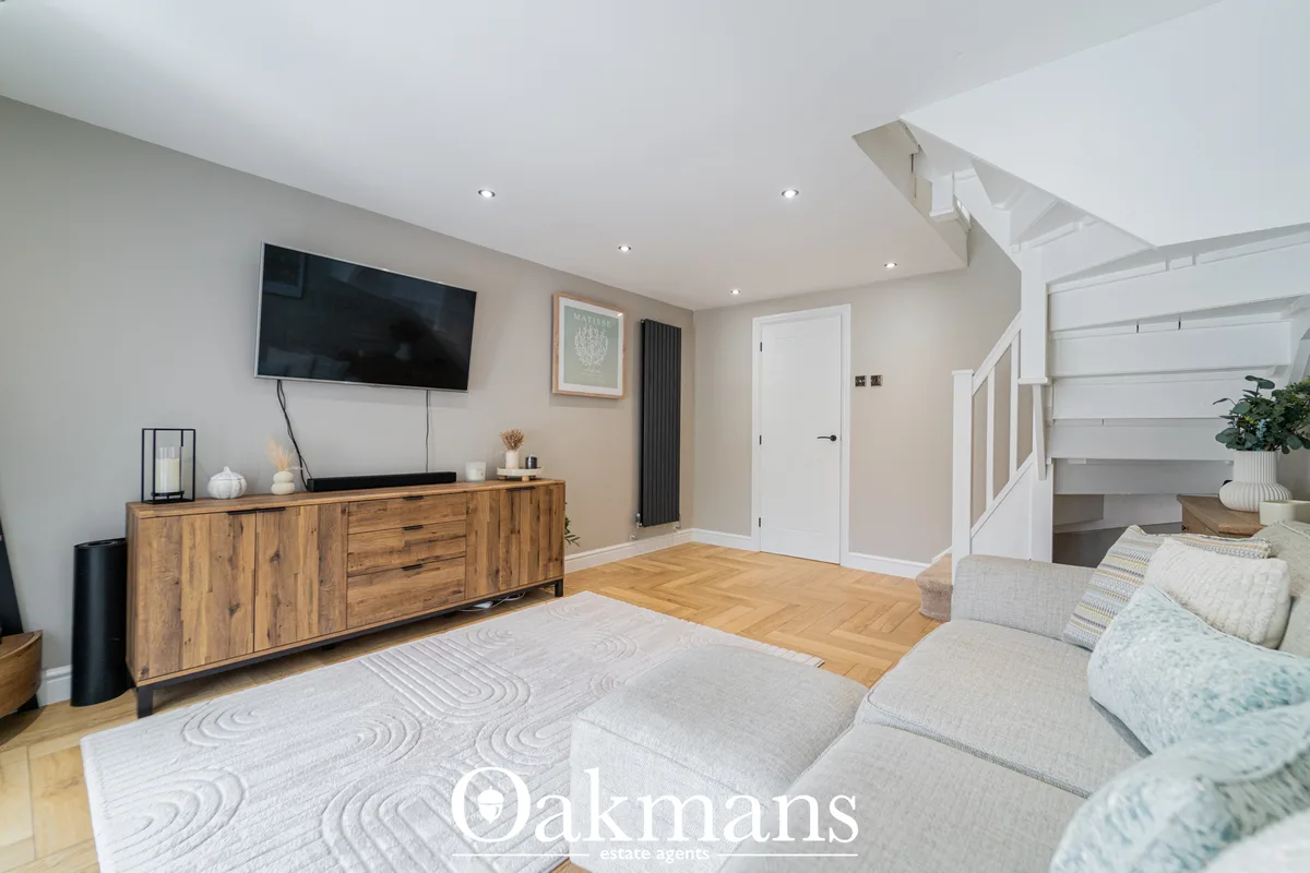 Spacious open-plan living room with cream walls, wooden media console, wall-mounted TV, grey upholstered sofa, geometric