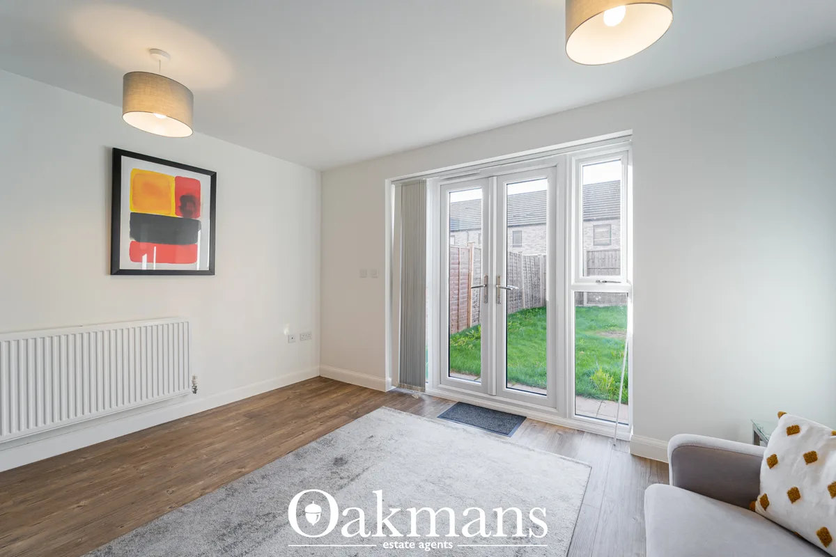 Bright living room with wooden flooring, white radiator, framed artwork, dual ceiling lights, and French doors opening t