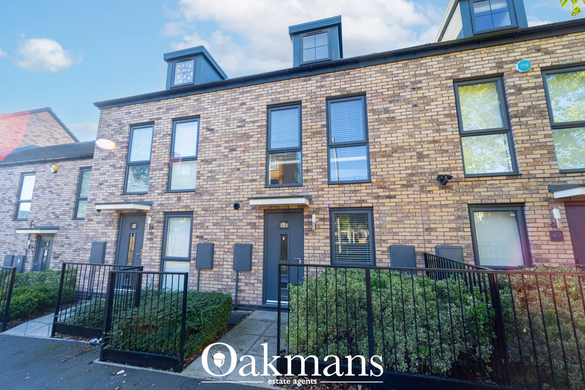 Modern brick townhouse with blue-framed dormer windows, black railings, and landscaped front garden on sunny day