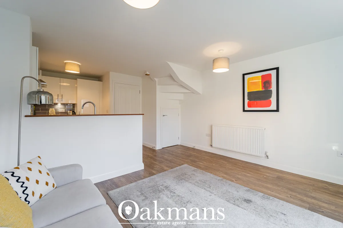 Open-plan living room with kitchen, wooden flooring, white radiator, framed artwork, ceiling lights and modern furnishin