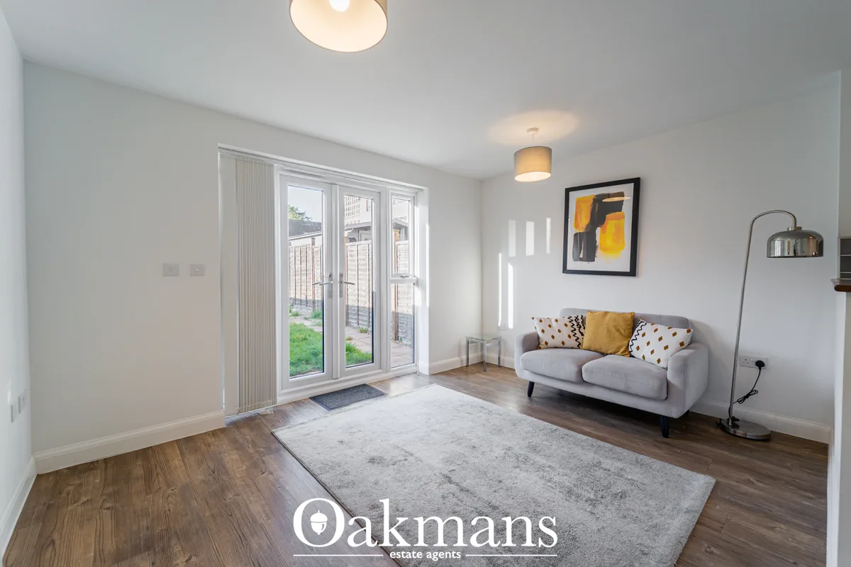 Bright living room with grey sofa, patterned cushions, wooden flooring, grey rug, glass patio doors, wall art and floor 