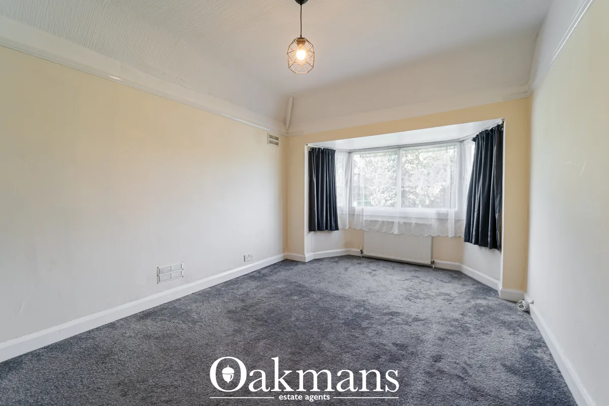 Spacious living room with cream and white walls, grey carpet, bay window with black curtains, pendant light, radiator an