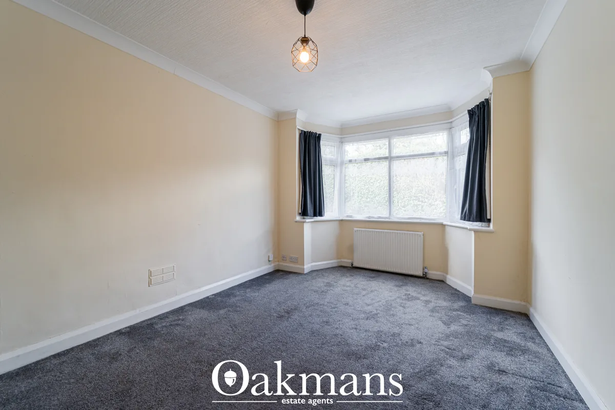 Spacious living room with bay window, grey carpet, cream and white walls, radiator, pendant light, dark curtains and whi