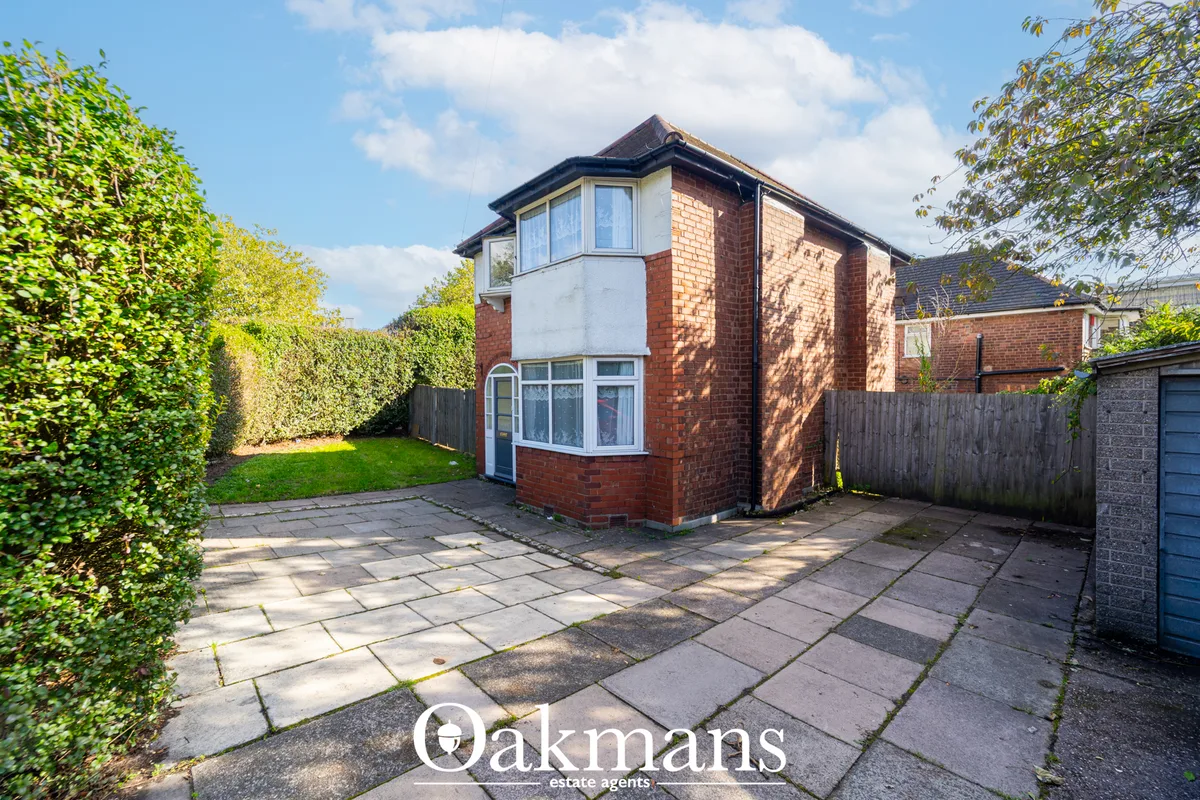 Red brick detached house with white render bay window, paved driveway, mature hedges, garage, clear blue sky