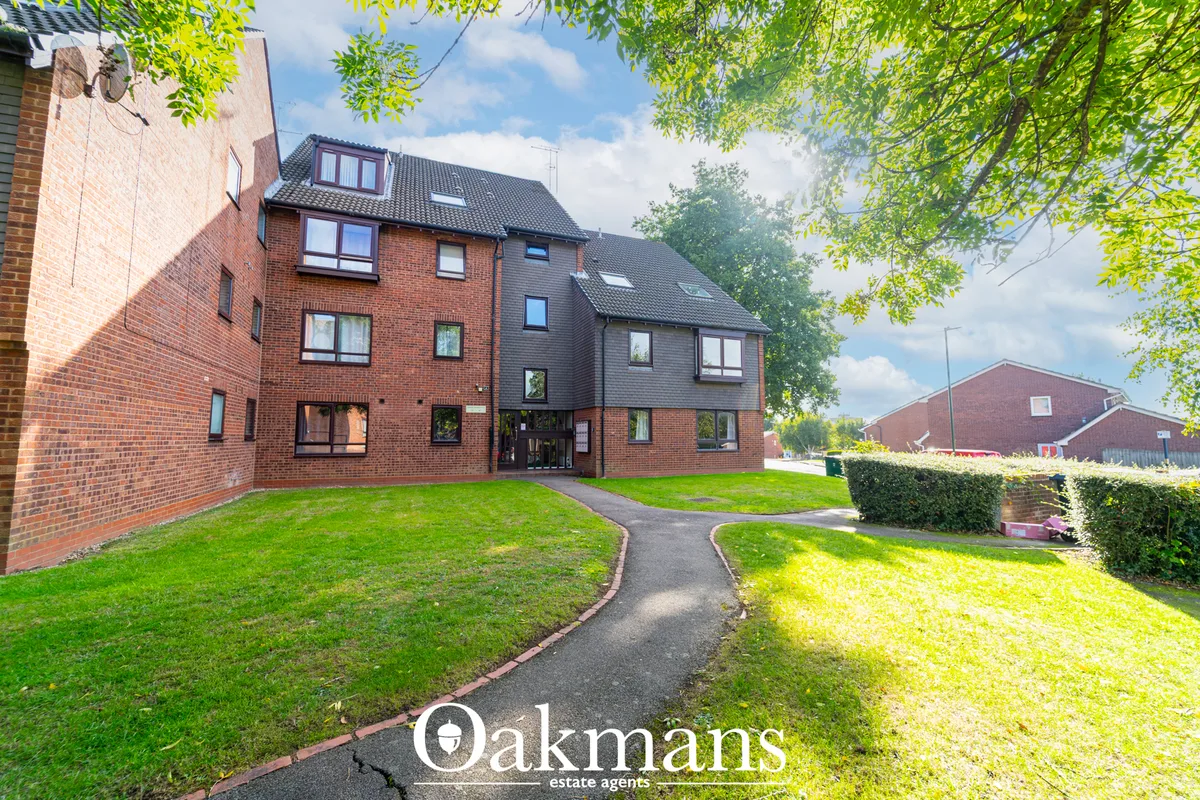 Red brick residential apartment building with manicured lawns, curved pathway, and mature trees overhead
