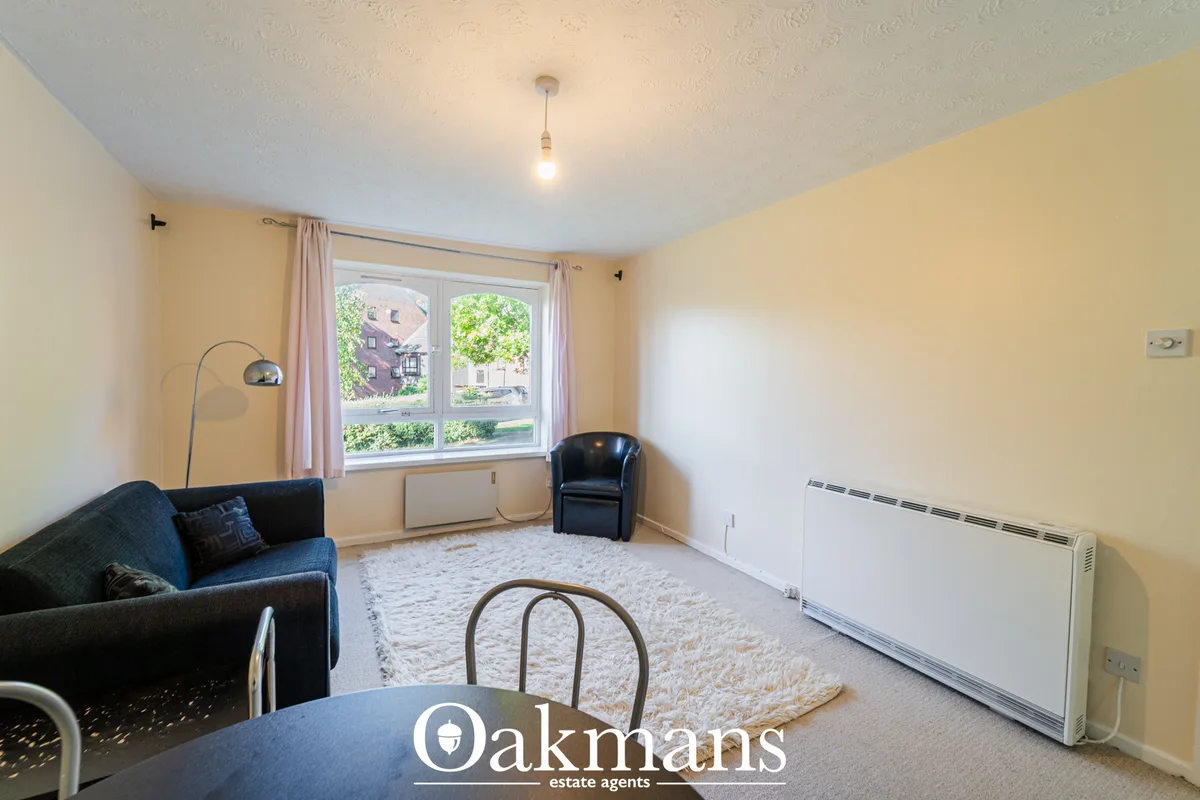 Bright living room with cream walls, large windows overlooking street, dark sofa, armchair, cream rug, pendant light and