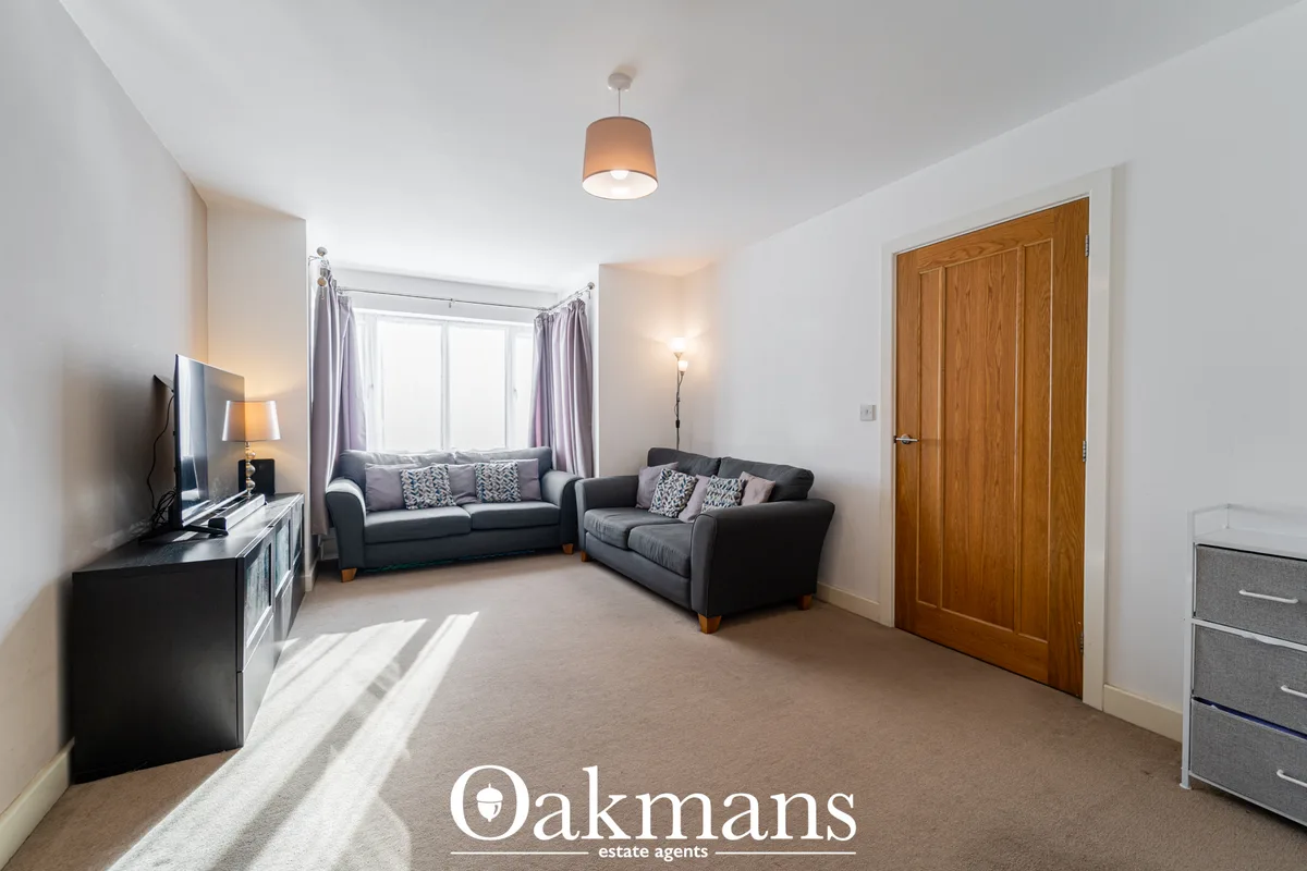 Bright living room with two grey sofas, large window with purple curtains, wooden door, TV, pendant light, and beige car