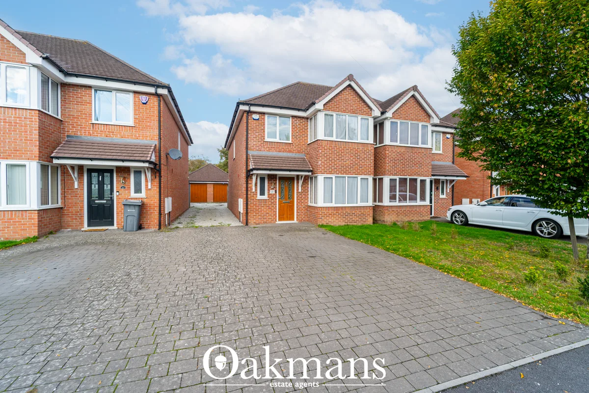 Row of modern brick-built residential properties with driveways, parked cars, and landscaped borders under blue sky