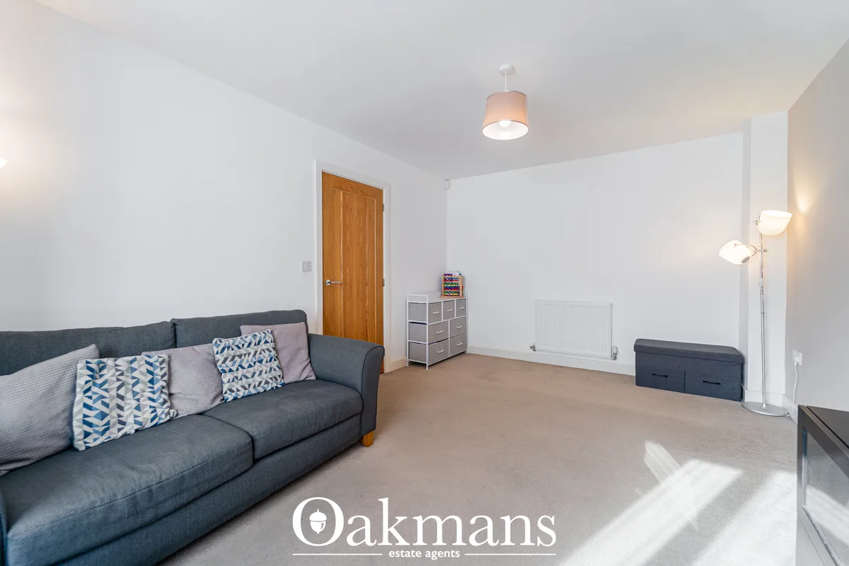 Spacious living room with charcoal sofa, patterned cushions, wooden door, storage unit, radiator and pendant lighting
