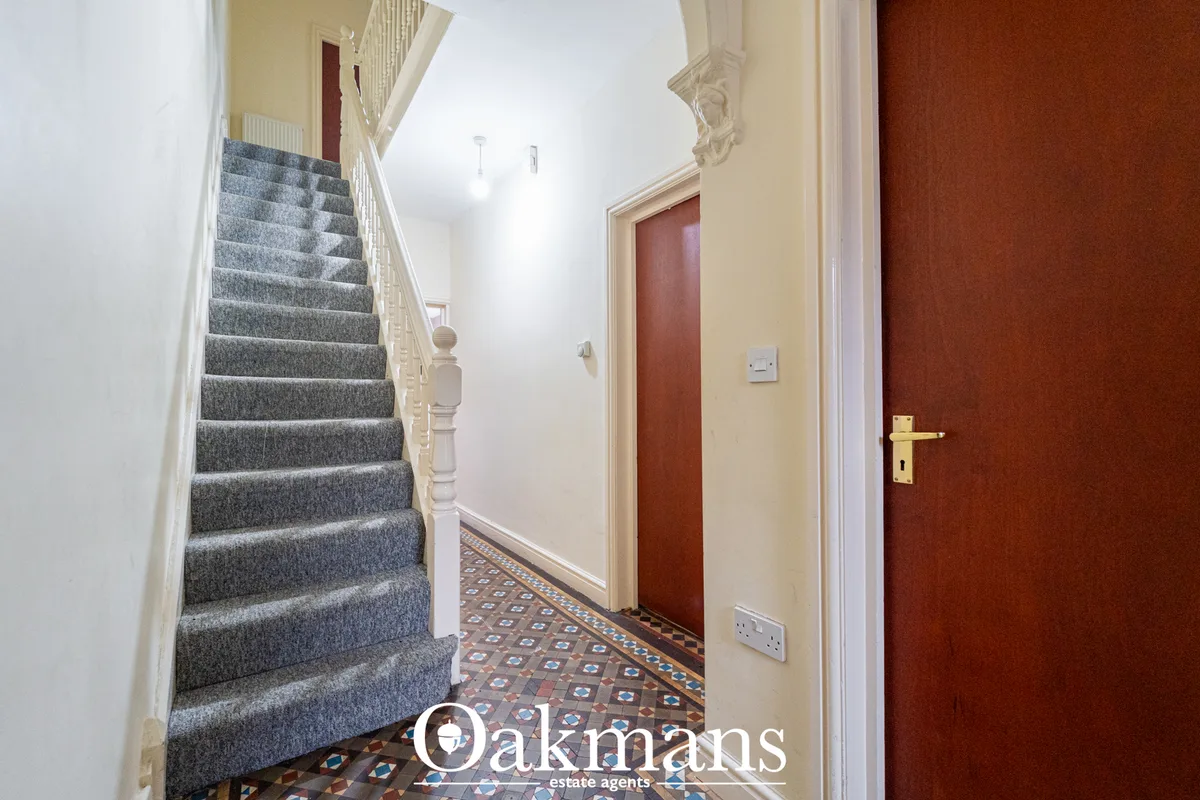 Entrance hallway with staircase to left, gray carpet, cream walls, red doors, ornate ceiling detail, geometric floor til