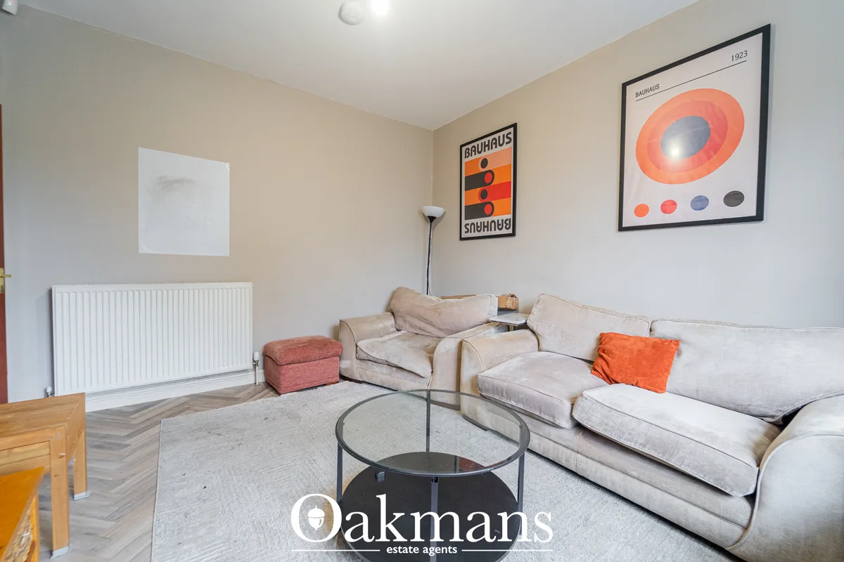 Spacious living room with beige L-shaped sofa, orange accent pillow, round glass coffee table, radiator and framed Bauha
