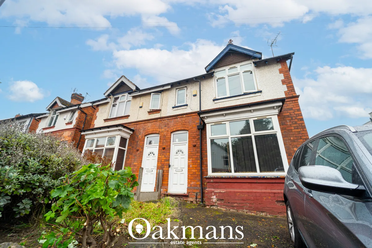 Red brick semi-detached house with cream upper storey, white doors and windows, parked car in driveway, hedges and blue 