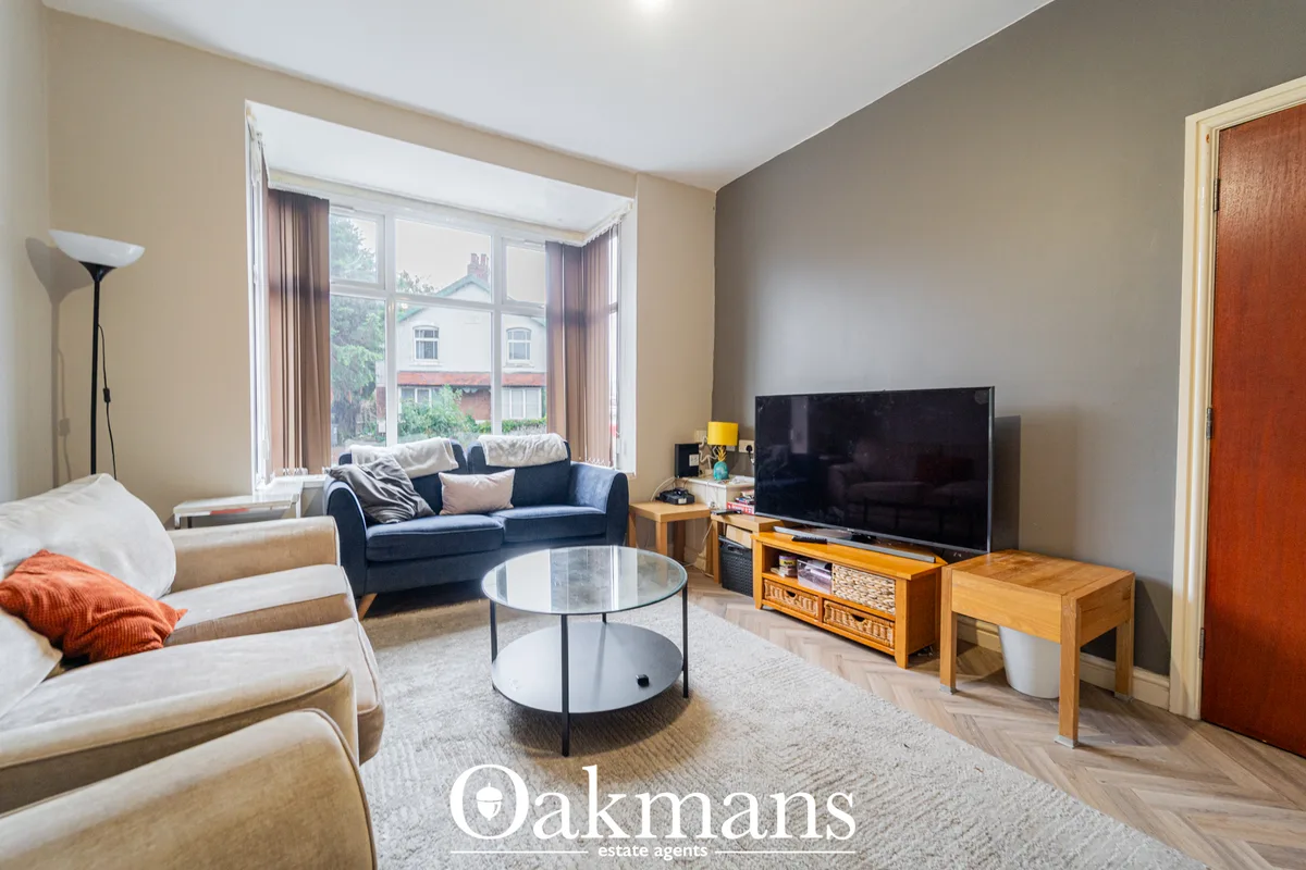 Bright living room with beige and grey walls, blue sofa, cream armchairs, wooden TV stand with flat-screen TV, round cof