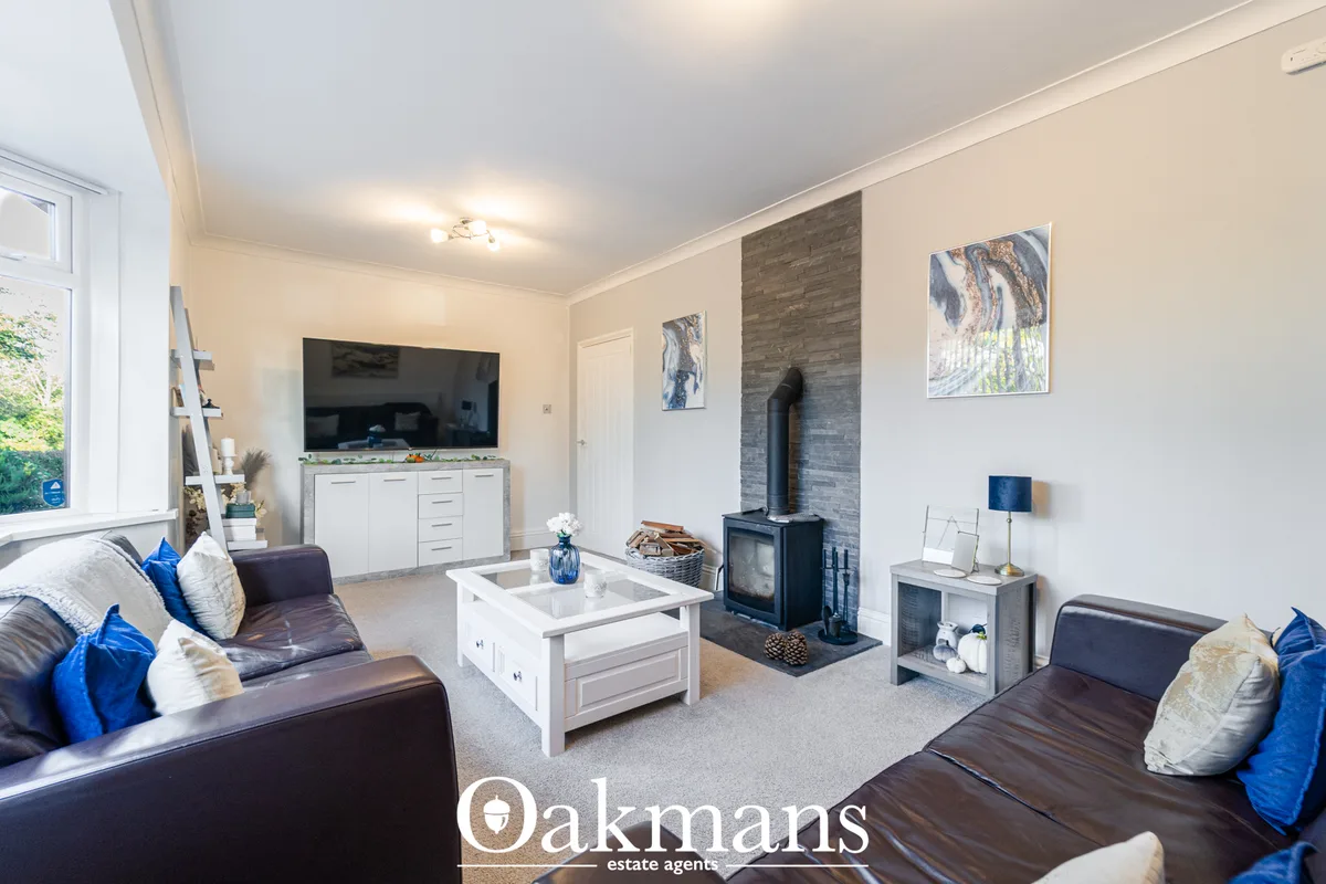 Spacious living room with dark leather sofas, white coffee table, wood-burning stove with grey brick surround, TV on whi