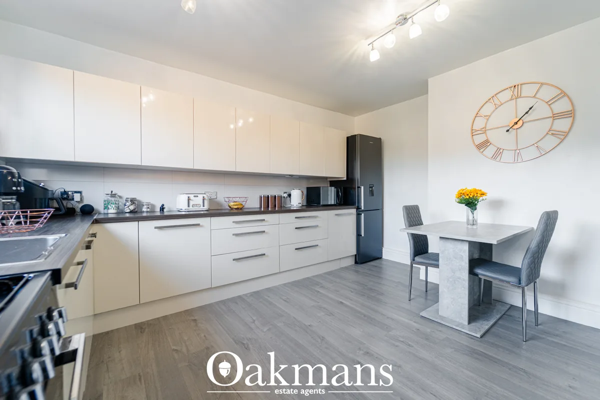 Modern fitted kitchen with white gloss units, dark grey worktops, black fridge-freezer, breakfast bar with grey upholste