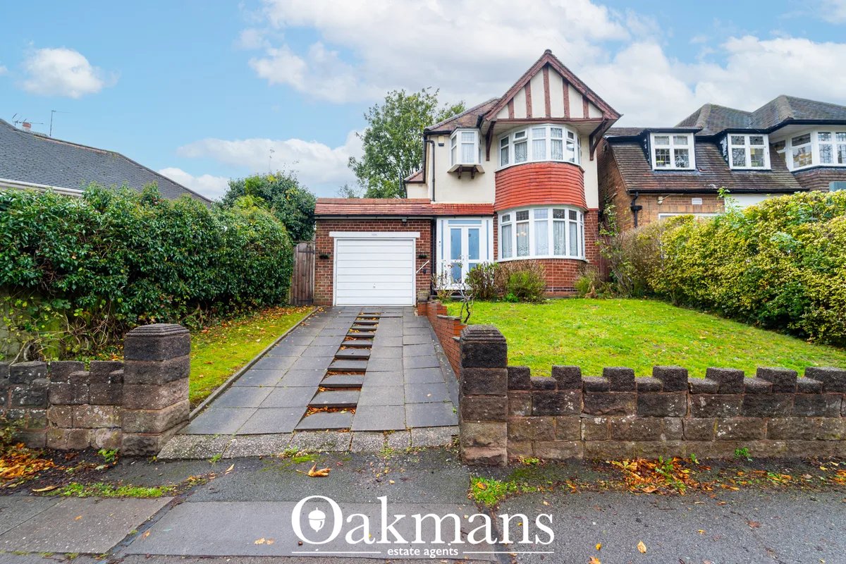 Detached red-brick house with white-painted timber gable, curved bay window, white garage door, block paved driveway and