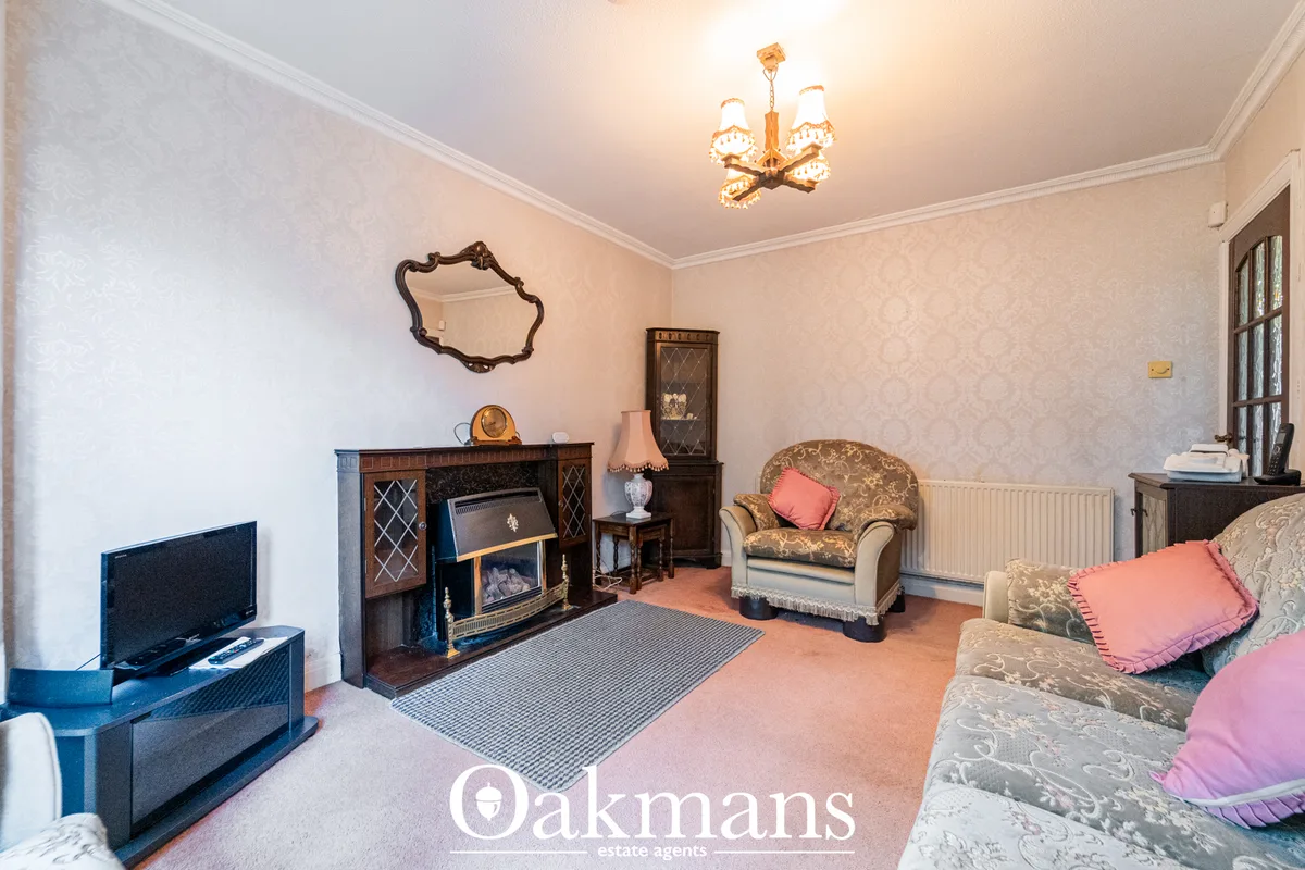 Spacious living room with fireplace, patterned wallpaper, cream upholstered armchair with pink cushions, period furnitur