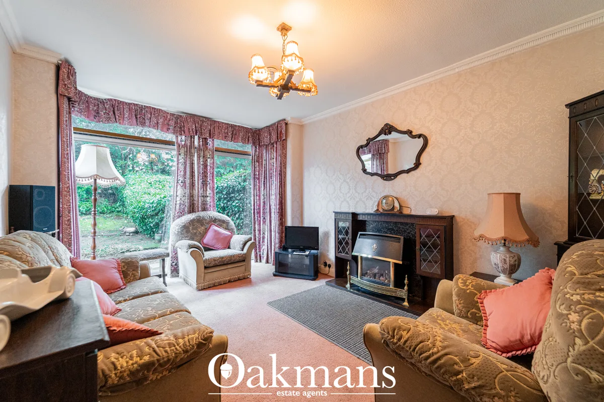 Elegant living room with period furnishings, decorative fireplace, bay windows with burgundy drapes, ornamental mirror, 