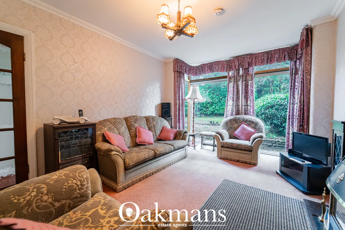 Spacious living room with traditional furnishings, patterned sofa and armchair, bay windows with burgundy curtains, chan