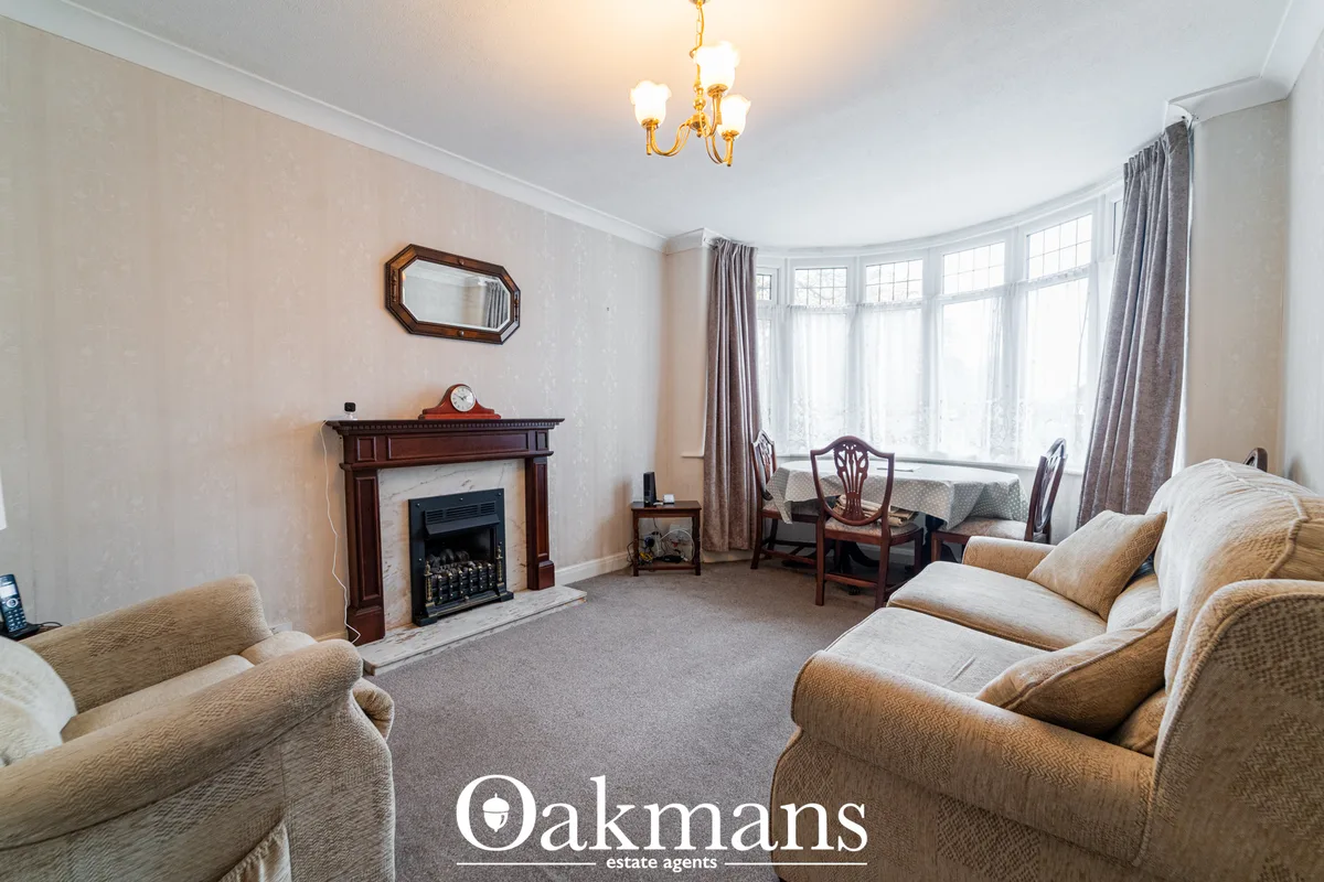 Spacious living room with cream textured wallpaper, beige upholstered seating, wooden fireplace with black insert, bay w