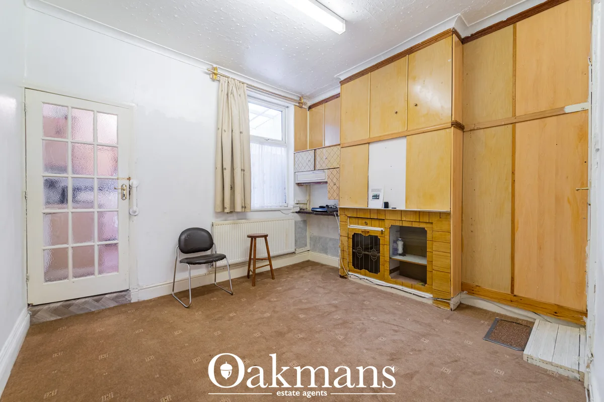 Kitchen with fitted wooden units, beige worktops, built-in oven, window with cream curtains, brown flooring and white te