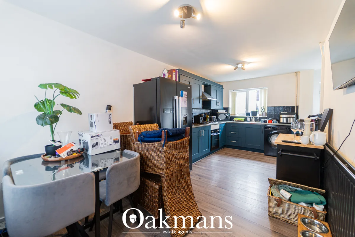 Open-plan living and kitchen area with dark blue cabinetry, wooden flooring, wicker furniture and potted plant