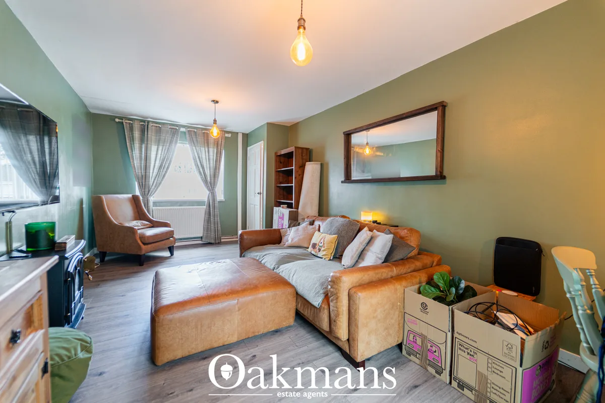 Spacious living room with tan leather sofa, armchair, wooden flooring, sage green walls, pendant lights and framed mirro
