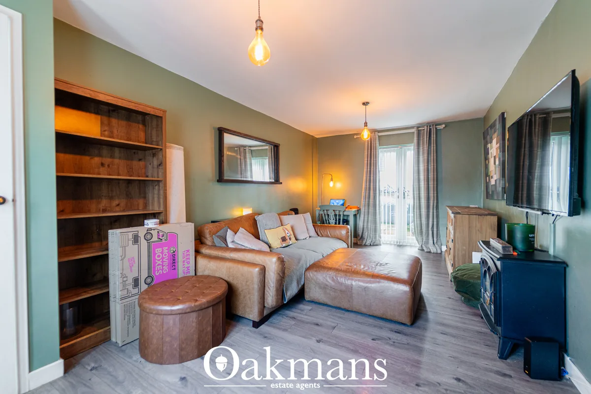 Spacious living room with tan leather sofa, wooden bookshelf, pendant lights, sage green walls, flat-screen TV, and acce
