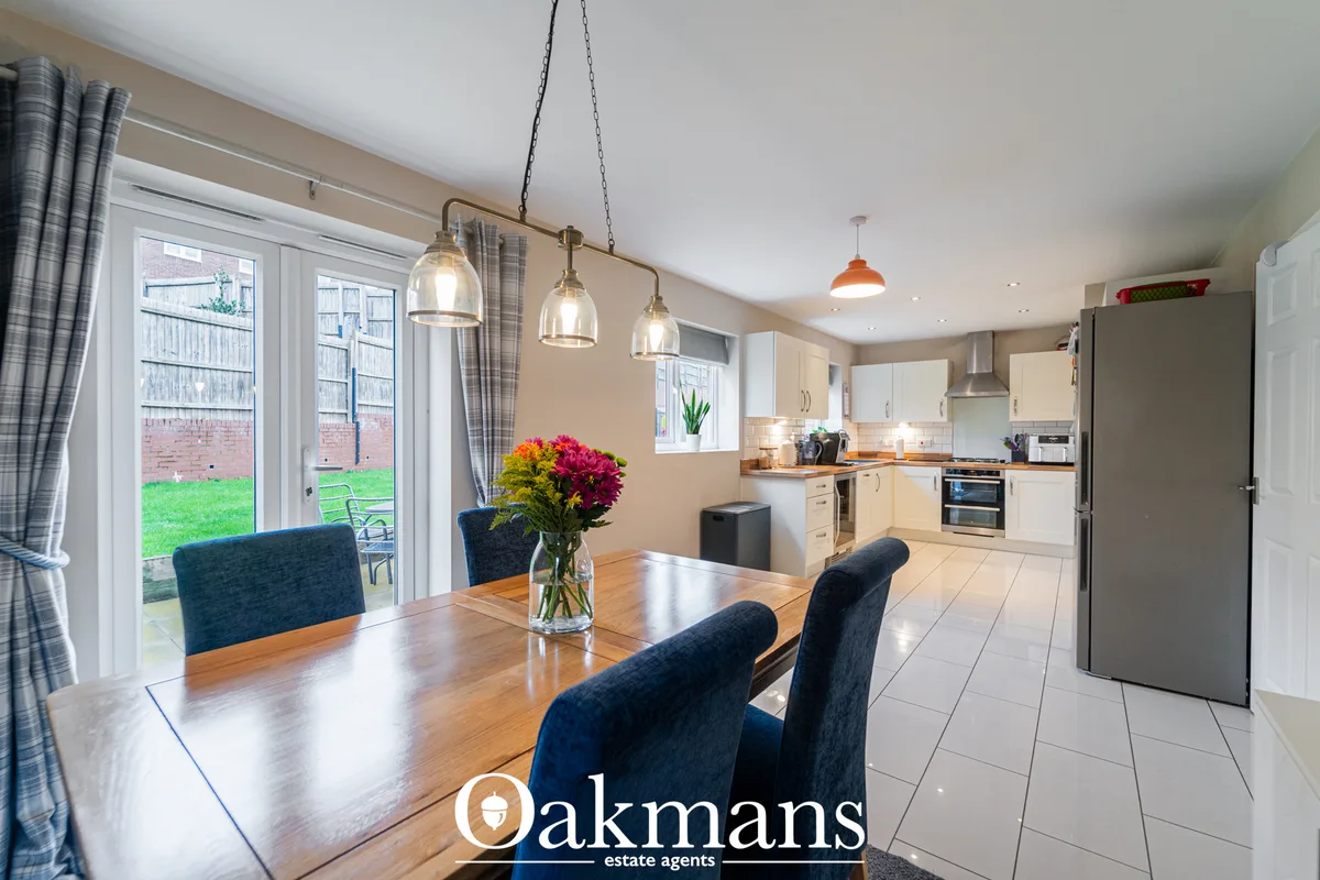 Open-plan dining room with wooden table, dark upholstered chairs, pendant lights, and garden views through patio doors