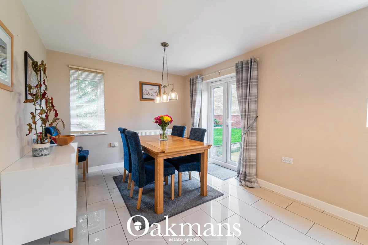 Spacious dining room with wooden table, blue upholstered chairs, pendant lighting, French doors to garden, peach walls a
