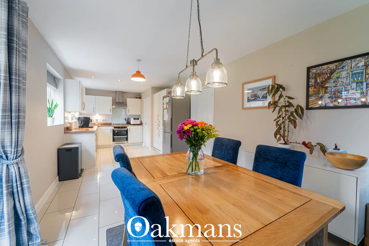 Open-plan dining room with wooden table, blue upholstered chairs, hanging glass pendant lights and fresh flowers in vase