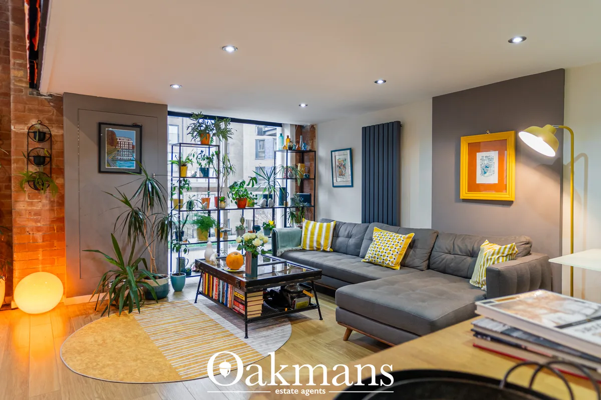 Contemporary living room with grey corner sofa, yellow accent pillows, black coffee table, potted plants, recessed light