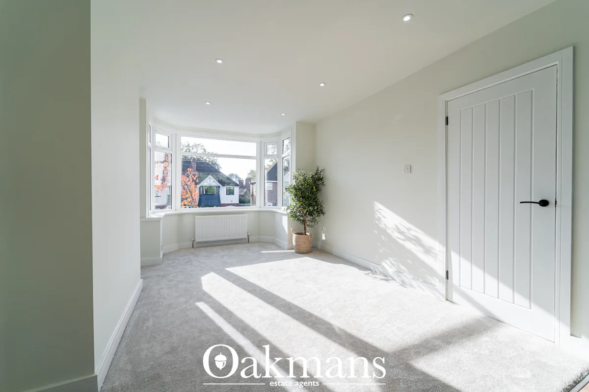 Bright modern bedroom with bay window, recessed ceiling lights, cream carpet, white built-in wardrobes, radiator and pot