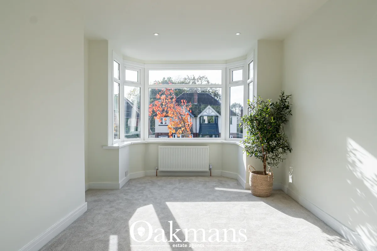 Bright conservatory with curved bay windows, grey carpet, white walls, radiator, potted plant, and views over residentia