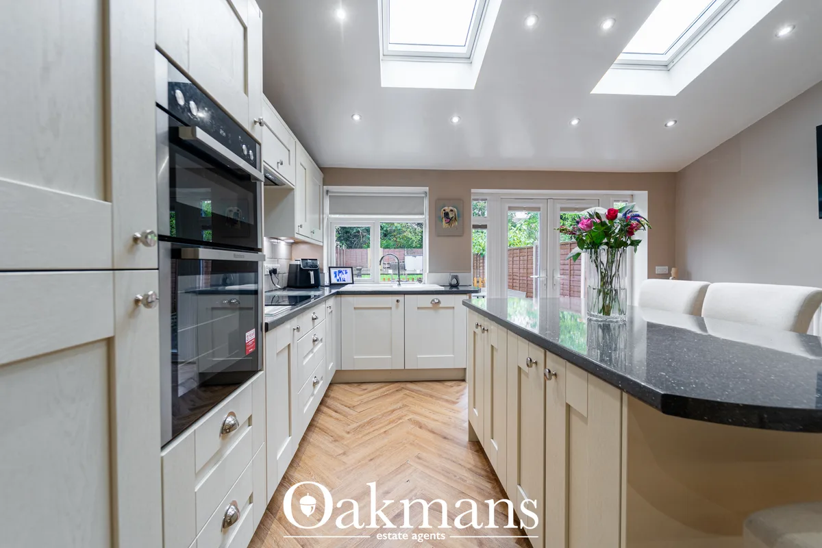 Modern fitted kitchen with white cabinetry, dark granite worktops, black integrated appliances, herringbone wood floorin