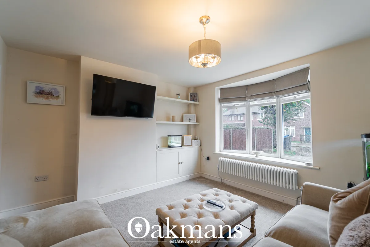 Bright living room with cream walls, wall-mounted TV, white shelving, large bay window with radiator, beige sofa, tufted