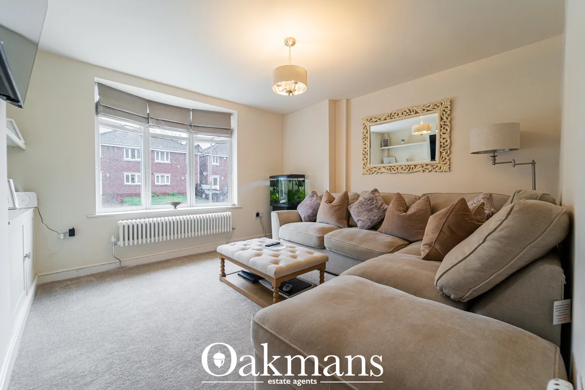 Spacious living room with beige sectional sofa, cream carpet, ornate mirror, pendant light, bay window with radiator and