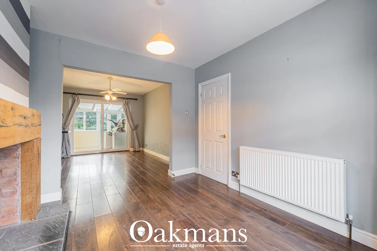 Bright hallway with wooden flooring, grey walls, white radiator, pendant light, white door and open doorway to living ar