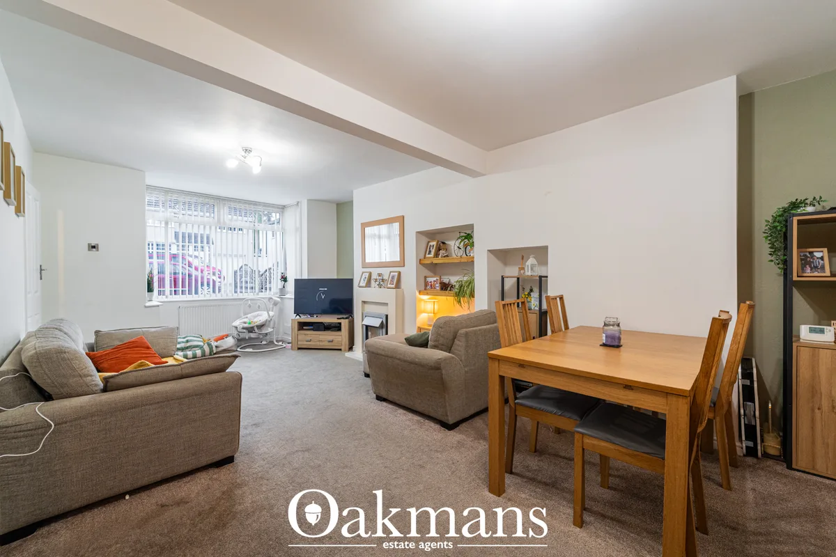 Spacious open-plan living and dining area with beige sofas, wooden dining table with chairs, built-in shelving, vertical