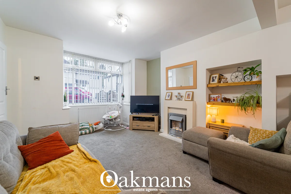 Spacious living room with beige carpet, grey corner sofa, TV unit with fireplace, shelving with decor, and large bay win
